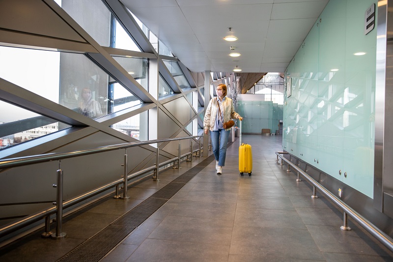 Passenger woman wearing a medical protective mask for prevent coronavirus walking with her luggage walking in almost airport/travel station. Travel ban, covid-19 outbreak.